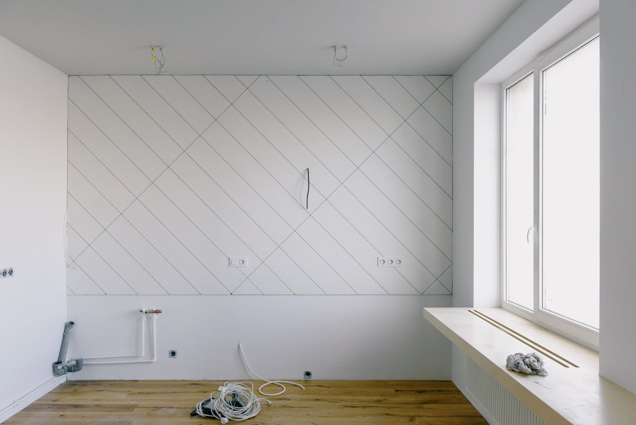 Modern room with renovation materials including cables and wooden floor, bright daylight streaming through the window.